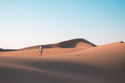 白天走在蓝天下的沙漠上的人